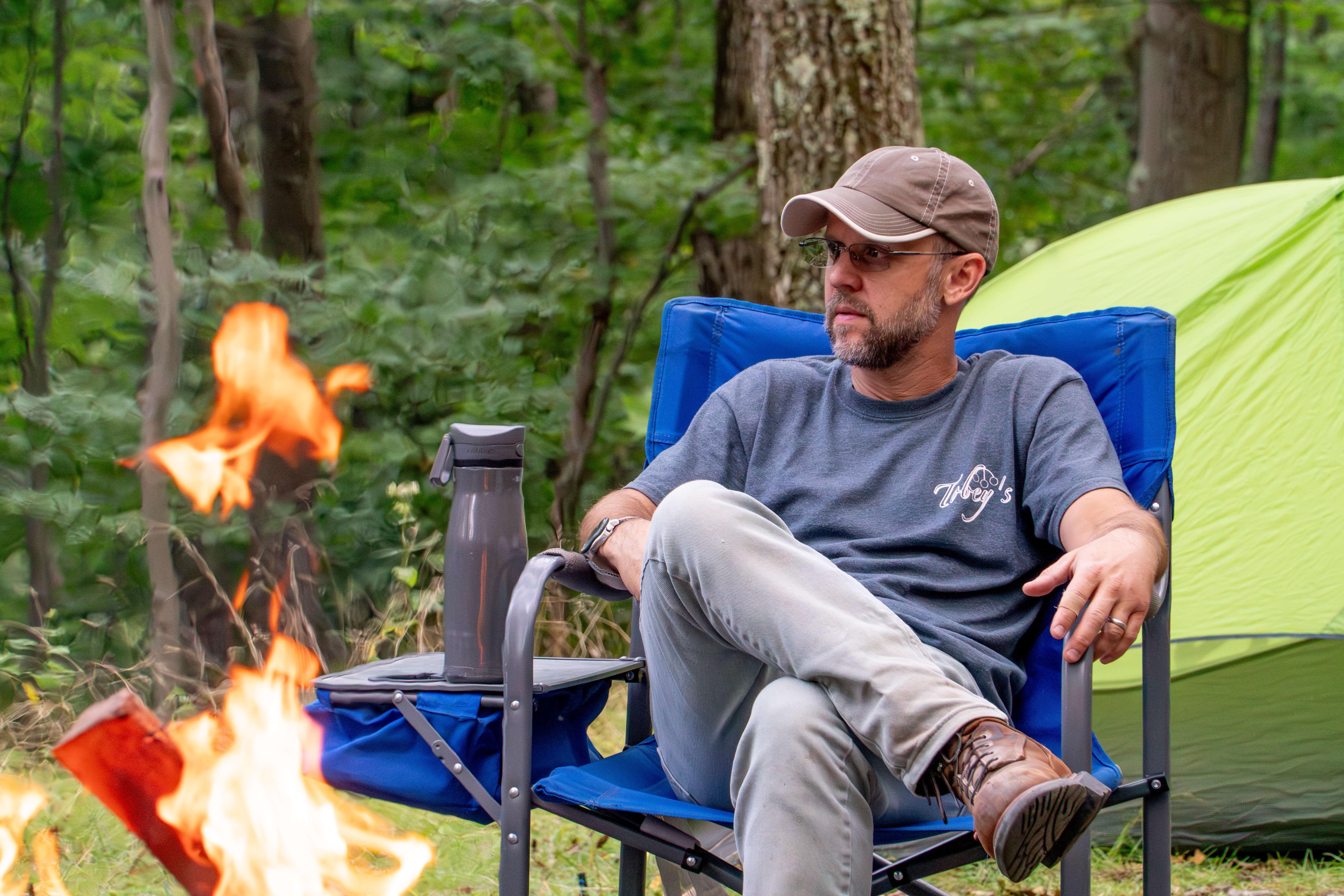 A guy sitting in a chair in front of a campfire.
