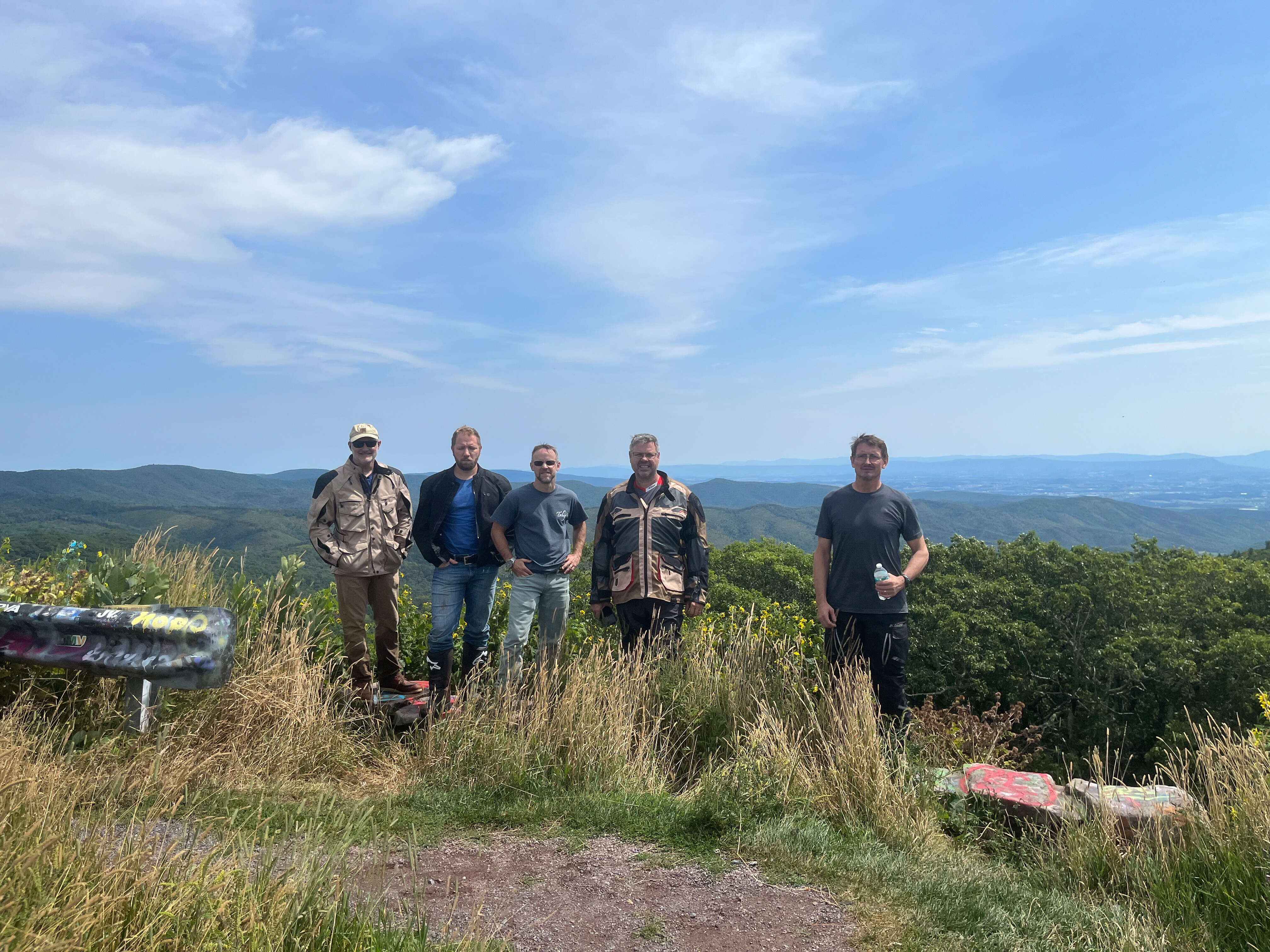 Guys standing on the edge of an overlook dressed in their motorcycle gear.