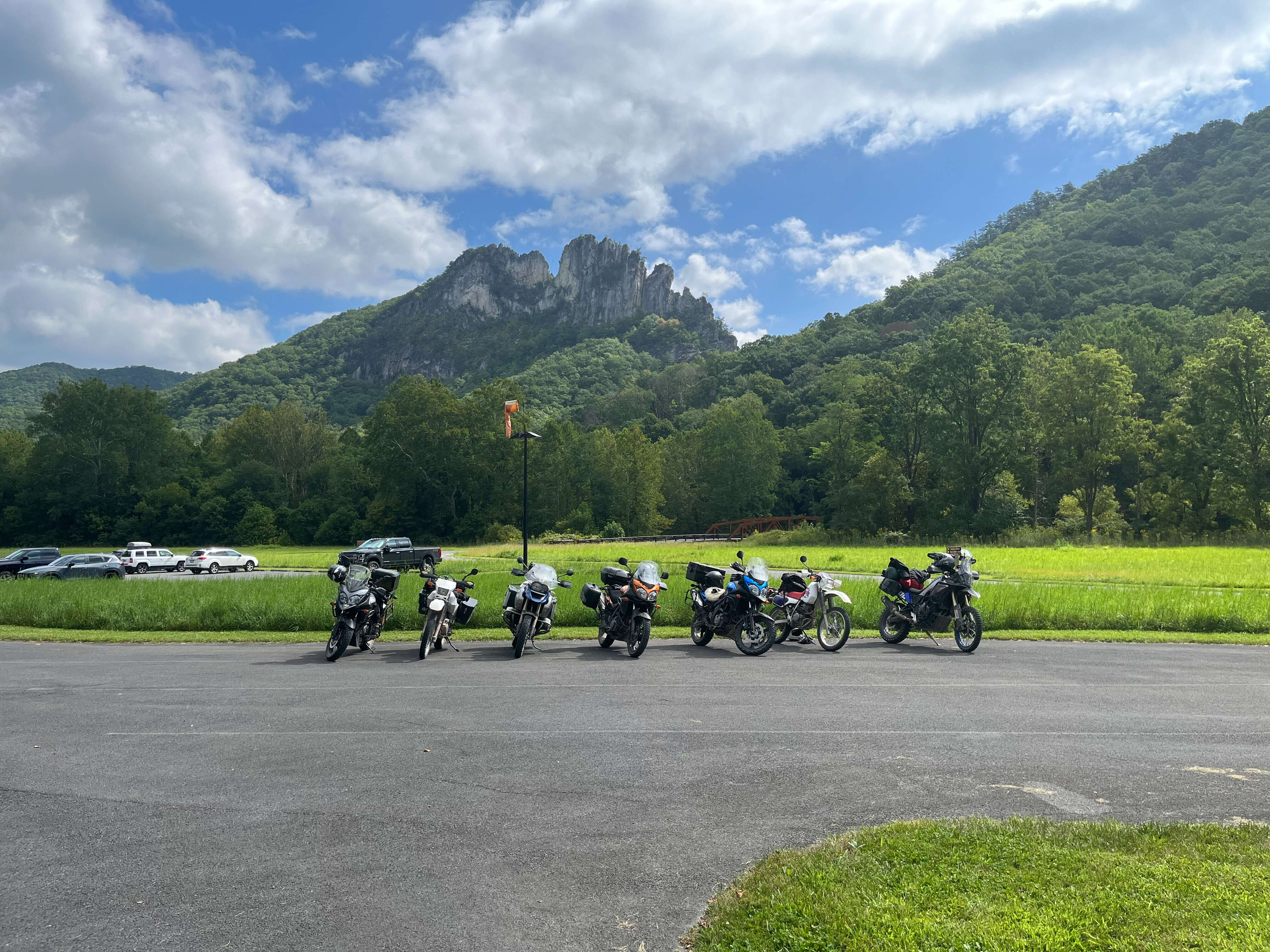 A line of motorcycles park in parking lot with Seneca Rocks in the background.